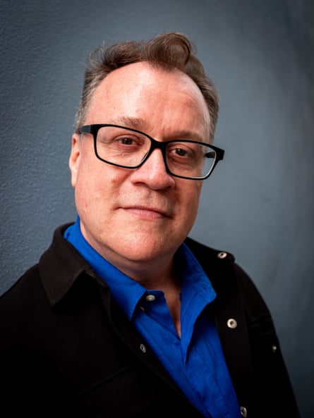 Close portrait of Davies with glasses, a dark blue shirt and dark jacket shot against a grey background
