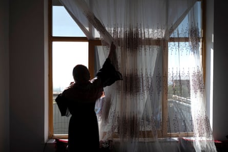 A woman pulls back a curtain to look out of a window