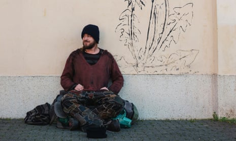 Homeless Man on street with graffiti on wall behind him