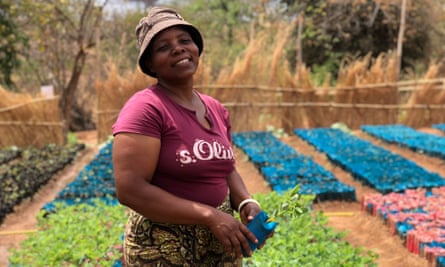 A smiling woman with vegetable plots behind.