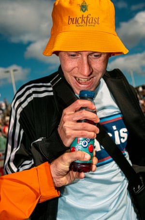 Fan singing into an Oasis soft drink bottle wearing a Buckfast tonic wine hat.