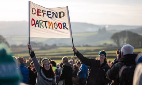Two people in a gathering hold up a banner saying 'Defend Dartmoor' with hills in the background