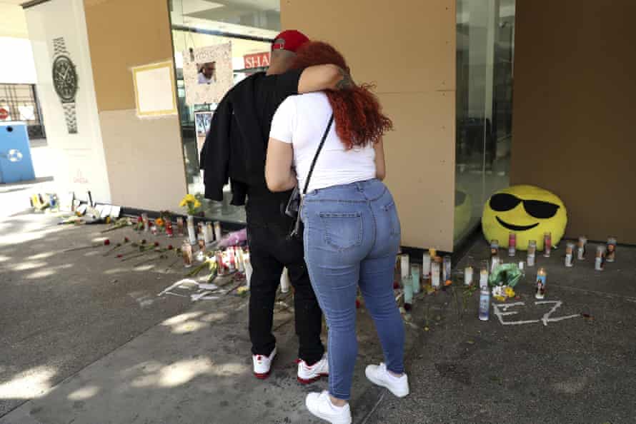 A couple hug in front of a memorial made up of candles, flowers and balloons.