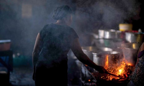 A woman cooks food over an open fire in a dimly lit kitchen