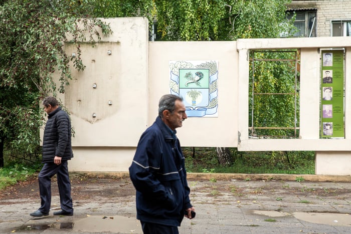Two men walk past a wall where a Ukrainian Trident was torn down
