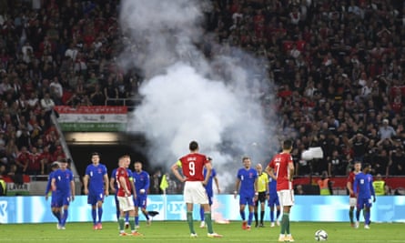 Players wait after a flare was thrown on the field following England’s third goal