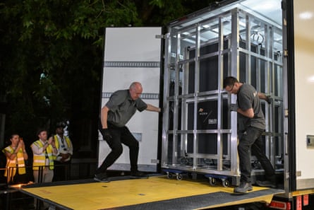 Two men pull the container on to a loading platform at the back of a lorry