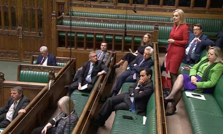 Liz Truss speaks in parliament during smoking ban debate – she is wearing a red dress and standing among a small cluster of other MPs in an otherwise empty-looking House of Commons