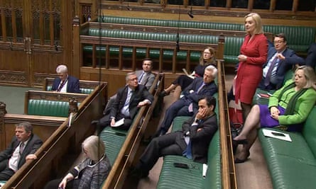Liz Truss speaks in parliament during smoking ban debate – she is wearing a red dress and standing among a small cluster of other MPs in an otherwise empty-looking House of Commons