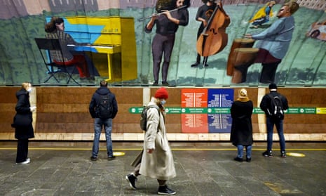 Commuters in Osokorky station of Kiev Metro in Ukraine last month. They stand over a large colourful mural of a band.
