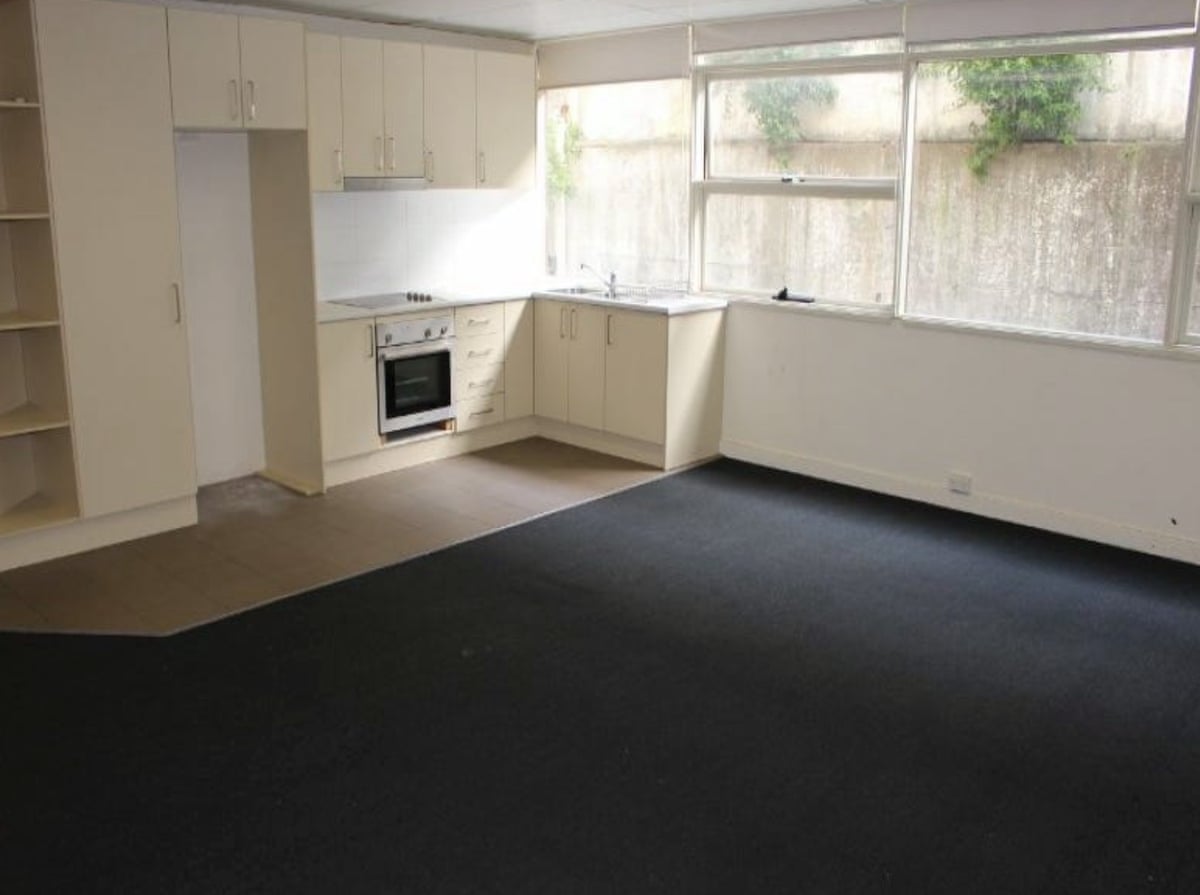 The kitchen and lounge room of a unit with windows that look out at a concrete wall