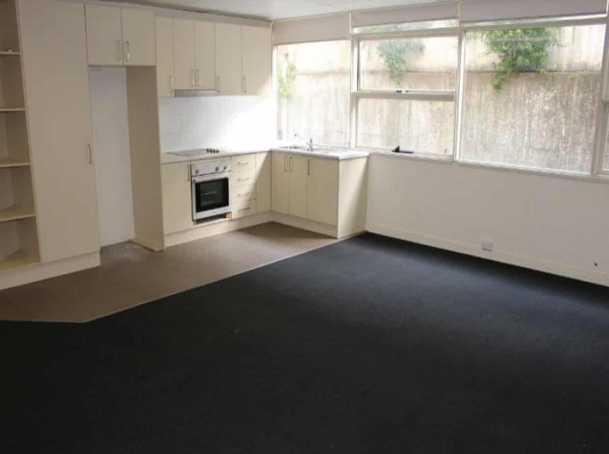 The kitchen and lounge room of a unit with windows that look out at a concrete wall