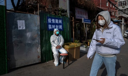 A woman wears a mask as she walks by an epidemic control worker as outside a locked-down community in Beijing.
