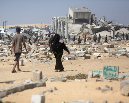 People walk past destroyed structures and scattered belongings
