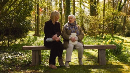 Whiley and Dench sit on a wooden bench on a sunny day, holding hot-water bottles and chatting