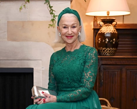 Helen Mirren smiles at the camera, wearing a green dress with a matching headband