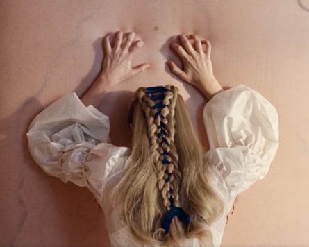 Margot Robbie seen from behind, scraping her fingernails down a flesh-coloured wall