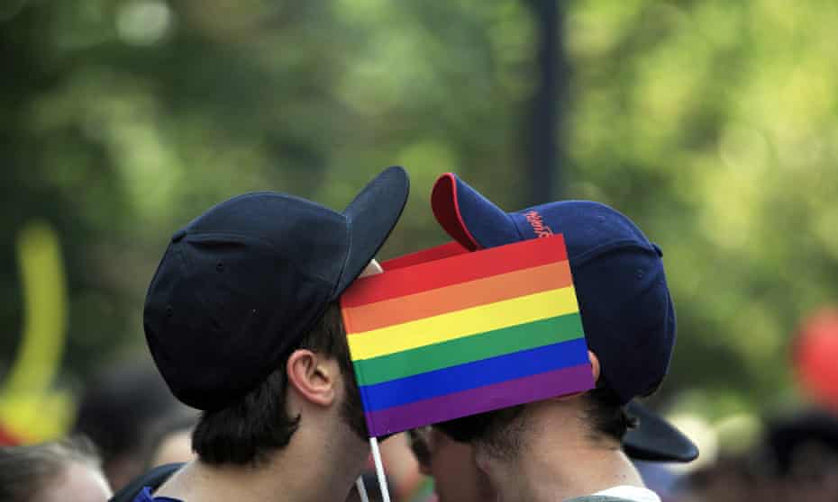 two men kiss behind a gay flag