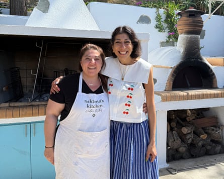 A smiling Georgina Hayden with her arm around a woman wearing a Nektaria’s Kitchen white apron in an outdoor kitchen