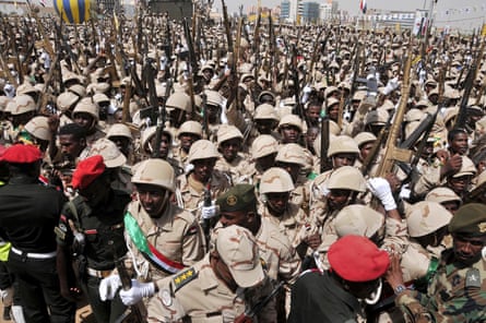 Men in new uniforms mass with their rifles in a large open space in a city