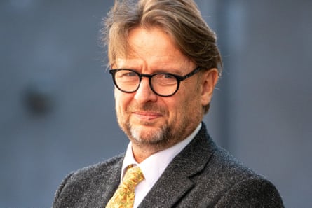 A headshot of a man wearing a suit and tie, and black-rim glasses.