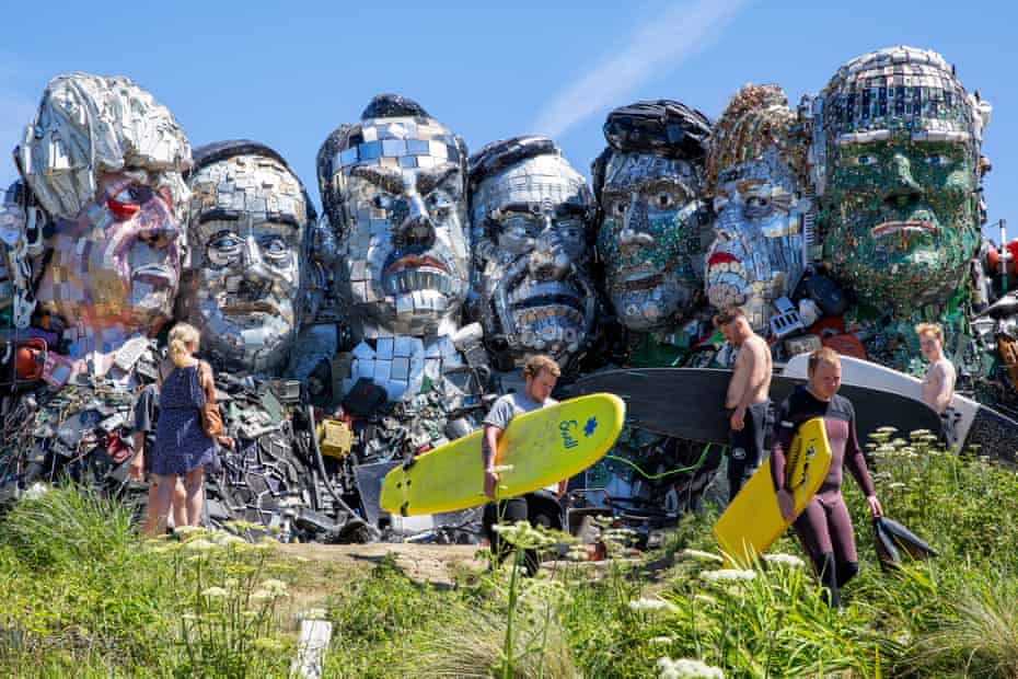 Surfers passing by 'Mount Recyclemore' in Hayle, a monument of the G7 leaders built from old technological waste