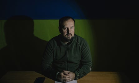 Andriy Besedin in darkened room with the flag of Ukraine on the the wall behind him