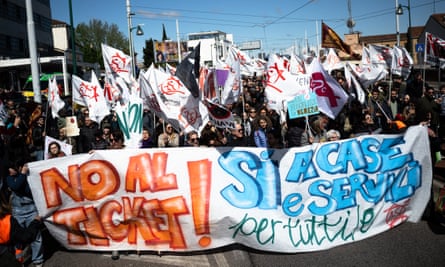 A group of protesters holding a large banner written in Italian, with other protesters holding small banners and flags behind