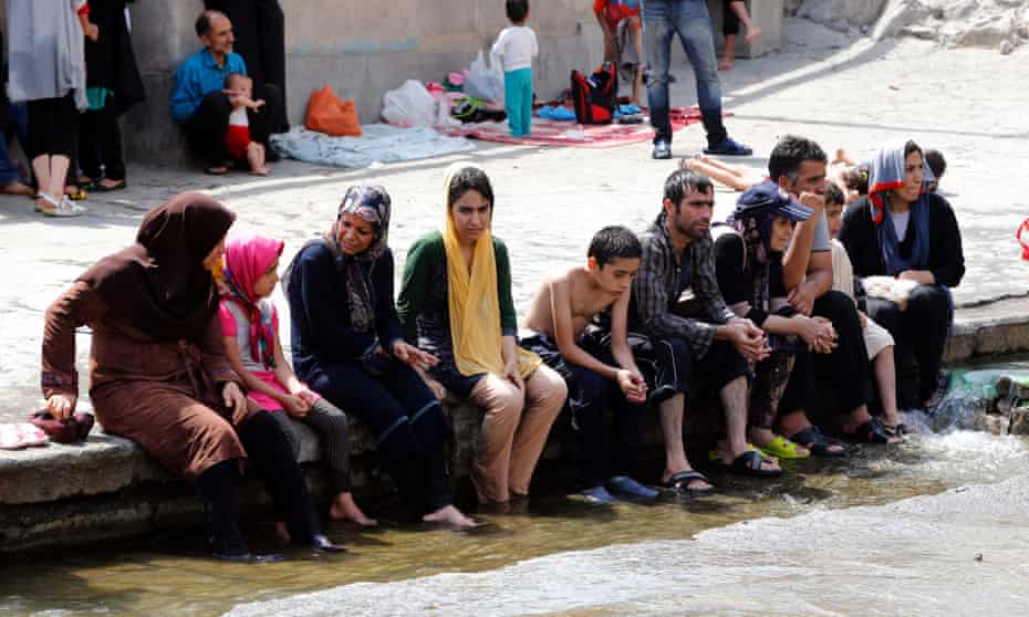 A group of Iranians sit with their feet in a pool.
