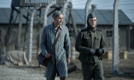 Two men walking alongside a wire fence in a scence from The Tattooist of Auschwitz   