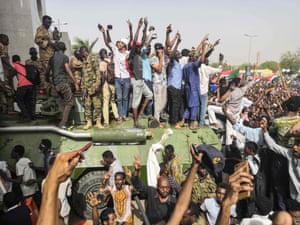 Demonstrators stand on an army armoured military vehicle as they cheer and flash the sign of victory