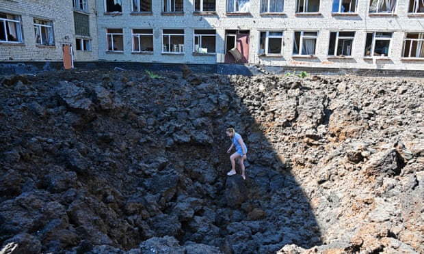 Una mujer se encuentra en un cráter causado por ataques con misiles que impactaron en el patio de una escuela en una zona residencial de Kharkiv en junio.
