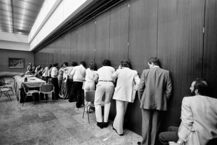 Black and white photo showing journalists in a meeting room listening at a wall in the 1980s.