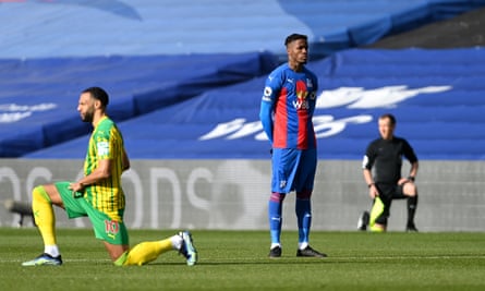 Wilfried Zaha stands while other players take a knee at Selhurst Park.