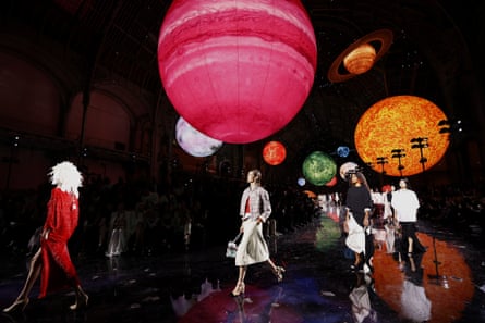 Models walking on the runway with model planets suspended overhead.