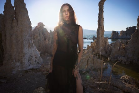 A woman in a black dress standing amid ragged rocks by the seaside
