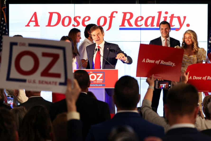 Mehmet Oz stands at a lectern speaking to a crowd of supporters. The sign behind him reads ‘A dose of reality’.