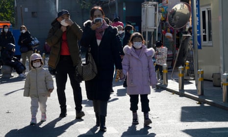 People including two young children wear face masks in the street outside a children’s hospital in Beijing, China, 24 November 2023.