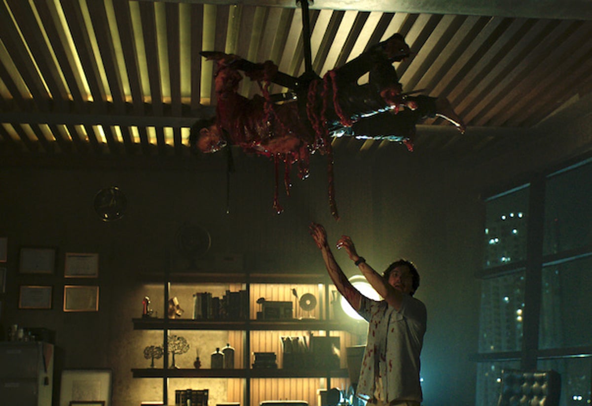 In Ghost in the Cell, a man reaches up towards a bloodied body hung upside down from the ceiling
