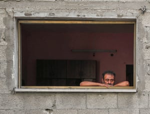 A man looks out of a blown-out window with wide eyes as Palestinians search for casualties of an overnight Israeli airstrike on a house at al-Shati refugee camp
