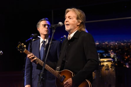 Paul McCartney with guitar and microphone standing next to Stephen Colbert on a stage
