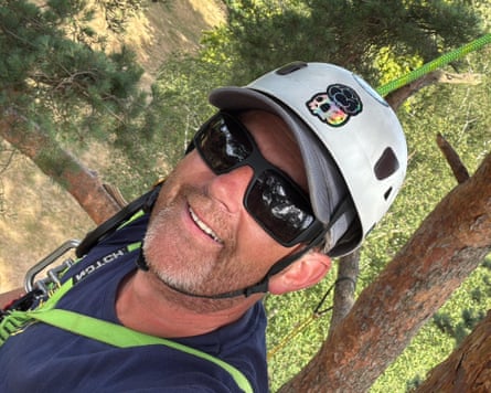 Jimmy Young with a white cap and sunglasses attached to a climbing rope with trees in the background