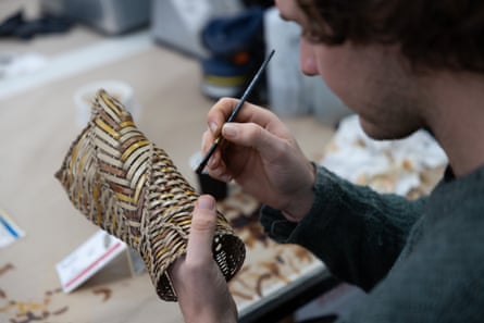 A close-up of hands painting a detailed woven limb with a small brush