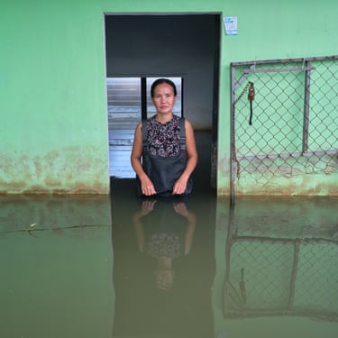 A woman stands in a doorway in a green wall waist-deep in flood water