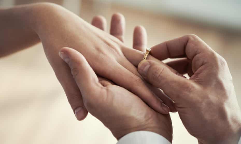 Close-up of a man placing a wedding ring on a woman's finger