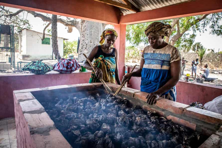 Duas mulheres estão sobre um grande poço de carvão com conchas de ostras
