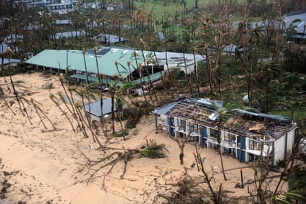 A beachside building with its roof torn off and palm trees stripped of fronds