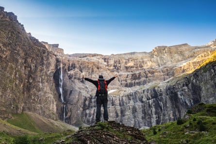 Man with arms outspread, waterfall, mountains rocky cliffs.