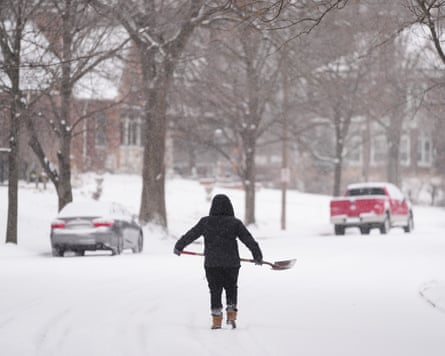 A person walks with a shovel down a snow-covered street during a winter storm in St Louis, Missouri.