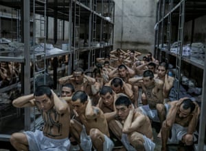 Prisoners wearing only shorts crouch with their hands over their heads